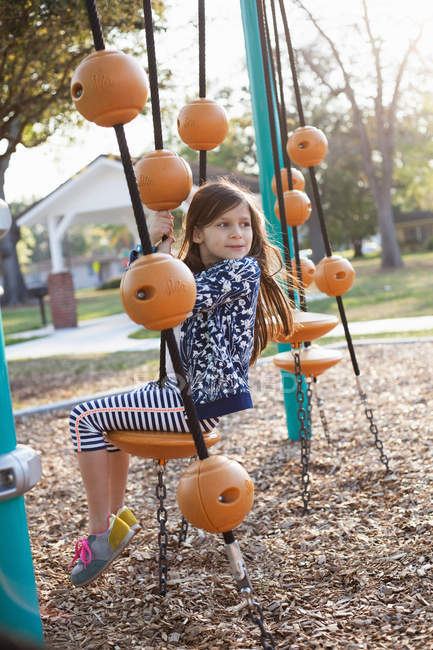 Vista lateral da menina sentada no balanço no parque infantil — Fotografia de Stock