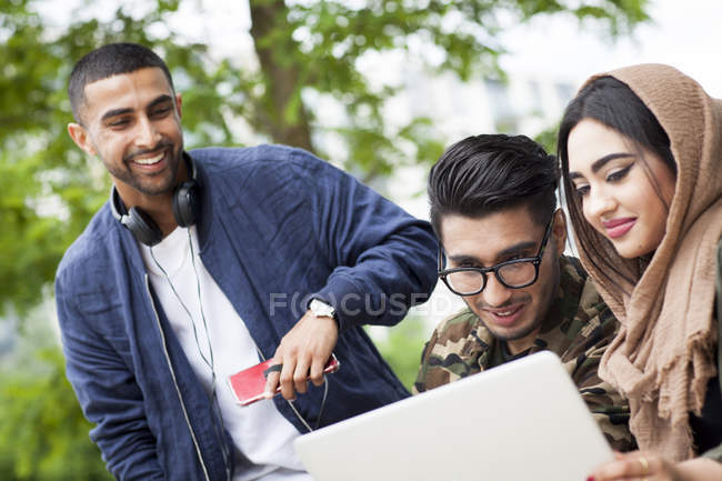 Tre amici che guardano il portatile all'aperto — Foto stock