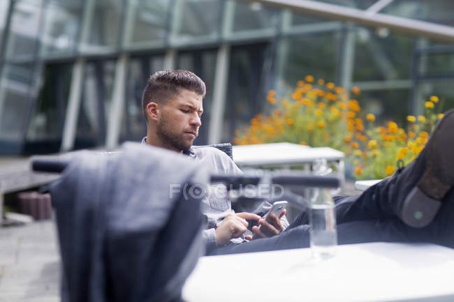 Homem com pés na mesa de mensagens de texto no smartphone — Fotografia de Stock