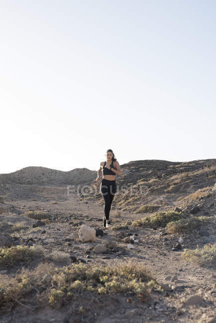 Jeune femme courant sur une piste de terre dans un paysage aride, Las Palmas, Îles Canaries, Espagne — Photo de stock