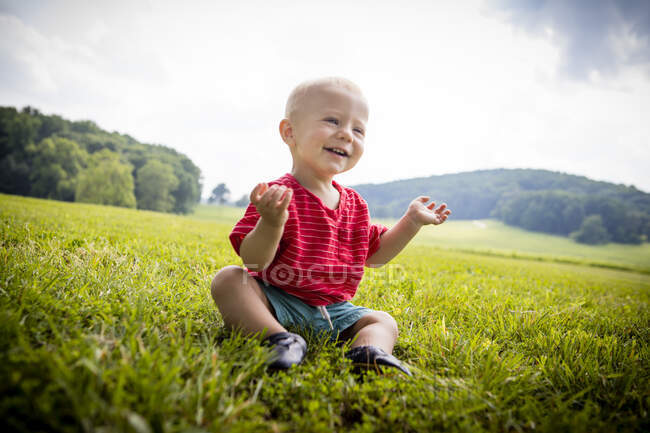 Niño feliz sentado en el campo rural - foto de stock