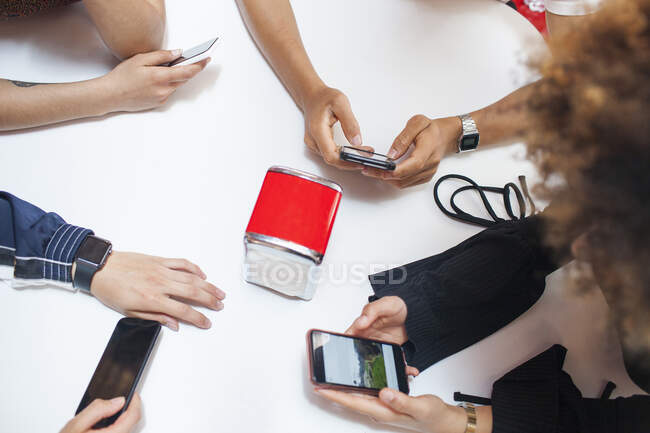 Group of young friends sitting at table, using smartphones, mid section — Stock Photo
