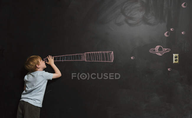 Мальчик смотрит в воображаемый телескоп, нарисованный на доске — стоковое фото