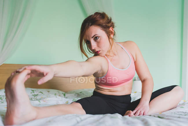 Jeune femme étirement et formation sur le lit — Photo de stock