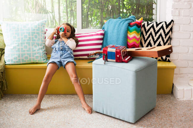 Retrato de menina inclinada no assento da janela fotografar com câmera de brinquedo — Fotografia de Stock