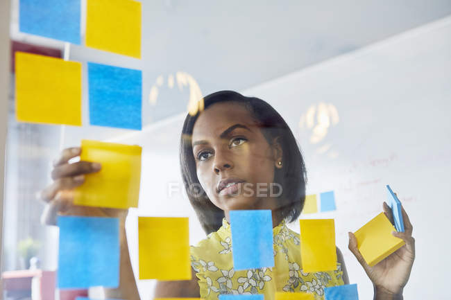 Молодая женщина в офисе прилипает записки к стеклу в офисе — стоковое фото