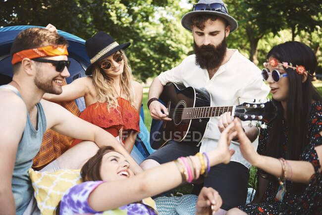 Fünf junge erwachsene Freunde spielen beim Festival-Zelten Akustikgitarre — Stockfoto