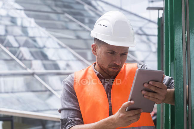Homem de chapéu duro e casaco de alta visibilidade usando tablet digital — Fotografia de Stock