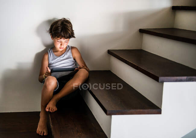Мальчик сидит на лестнице и смотрит на цифровой планшет — стоковое фото