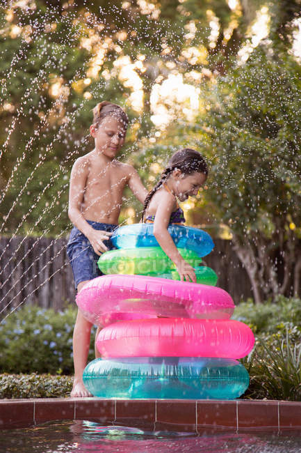 Young girl and boy having fun with inflatable rings at outdoor swimming pool — Stock Photo