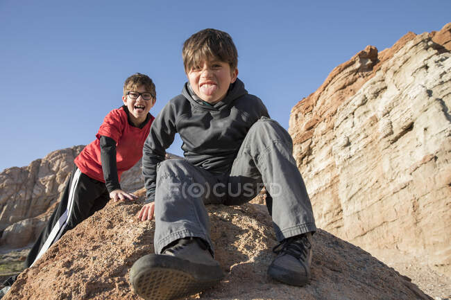 Porträt von Jungen, die auf einem Felsen sitzen und in die Kamera schauen und die Zunge herausstrecken, Lone Pine, Kalifornien, USA — Stockfoto