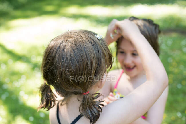 Young girl putting daisies in sister's hair, outdoors — Stock Photo
