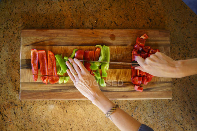 Обрезанный образ женщины, рубящей красный и зеленый перец на кухне — стоковое фото