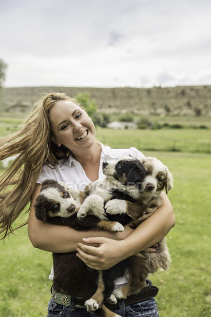 Portrait of young woman carrying three puppies in arms on ranch, Bridger, Montana, USA — Stock Photo