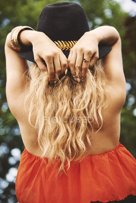 Visão traseira da jovem mulher boho em trilby com as mãos atrás da cabeça no festival — Fotografia de Stock