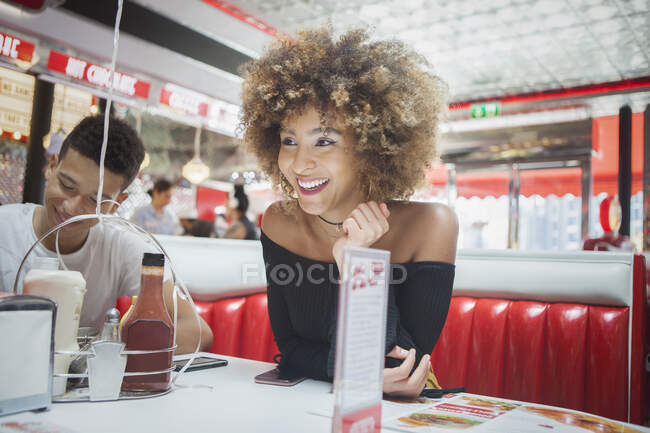 Друзья сидят в закусочной, молодая женщина смотрит в сторону, улыбаясь — стоковое фото
