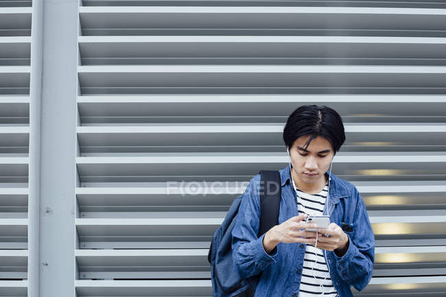 Jeune homme dans les écouteurs en utilisant smartphone à l'extérieur — Photo de stock