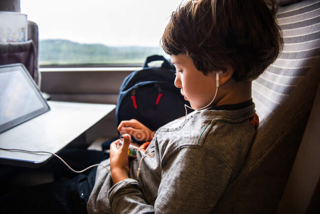 Young boy travelling on train, using digital tablet, wearing earphones — Stock Photo
