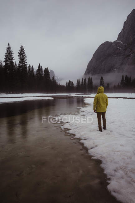 Vue arrière d'un randonneur masculin surplombant un paysage enneigé et une rivière, Yosemite Village, Californie, États-Unis — Photo de stock