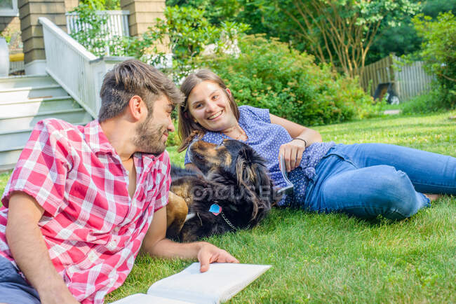 Pareja en la hierba en el jardín con el perro, leyendo - foto de stock