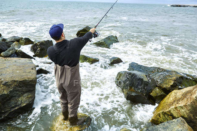 Молодий чоловік стоїть на скелястій морській риболовлі — стокове фото