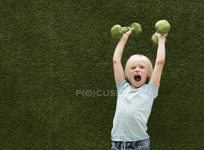 Мальчик перед искусственной травой поднимает гантели — стоковое фото