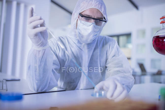 Trabajador de laboratorio usando pipeta larga, dejando caer líquido en la placa de Petri - foto de stock