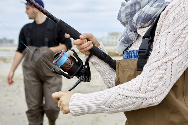 Mujer en vadeadores bobinado carrete de pesca en la playa - foto de stock