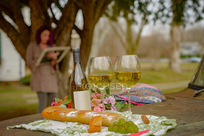 Стіл з пляшкою вина, окулярами та їжею на відкритому повітрі та жінкою на фоні — стокове фото