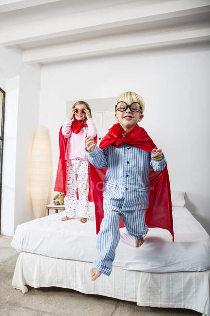 Menino e fêmea gêmea em capas vermelhas pulando da cama — Fotografia de Stock