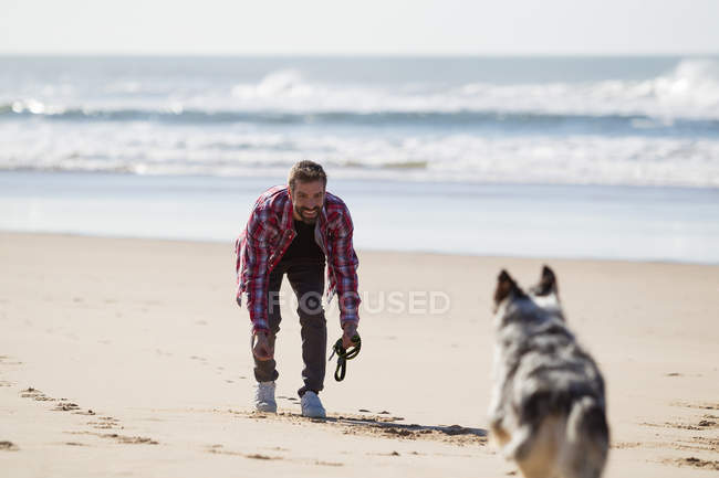 Uomo che gioca con il cane sulla spiaggia di sabbia — Foto stock