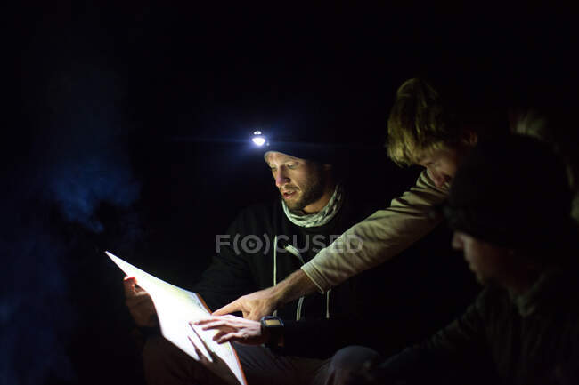 Three men looking at map, at night, using headlamp for light — Stock Photo