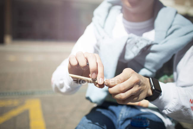 Vista sezione centrale di Giovane uomo rotolamento sigaretta seduta all'aperto — Foto stock