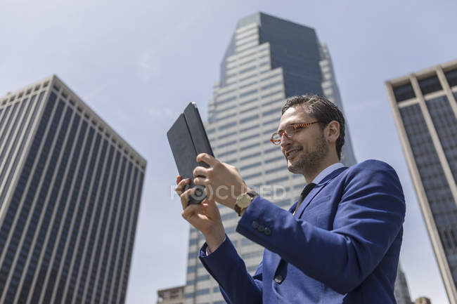 Homme d'affaires regardant tablette numérique à côté des gratte-ciel — Photo de stock