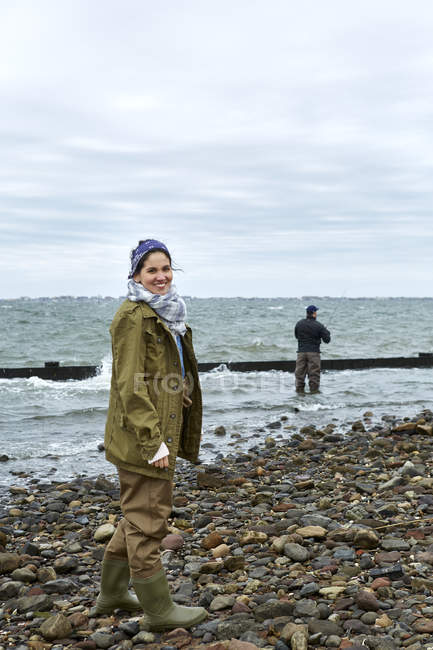 Retrato de mulher jovem na praia enquanto namorado pesca — Fotografia de Stock