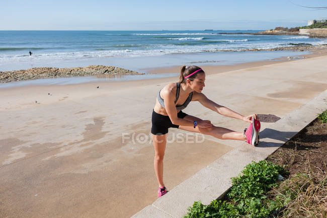 Junge Frau wärmt sich auf und dehnt sich am Strand, carcavelos, lisboa, portugal, europa — Stockfoto