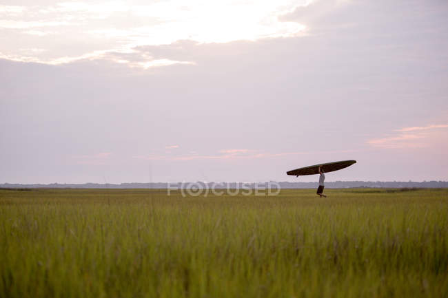 Side view of man carrying surfboard in green field — Stock Photo