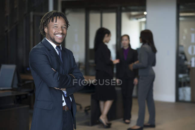 Porträt eines Geschäftsmannes, während Geschäftsfrauen im Hintergrund reden — Stockfoto