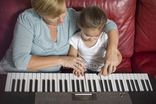 Mädchen und Großmutter spielen Keyboard auf dem Sofa — Stockfoto