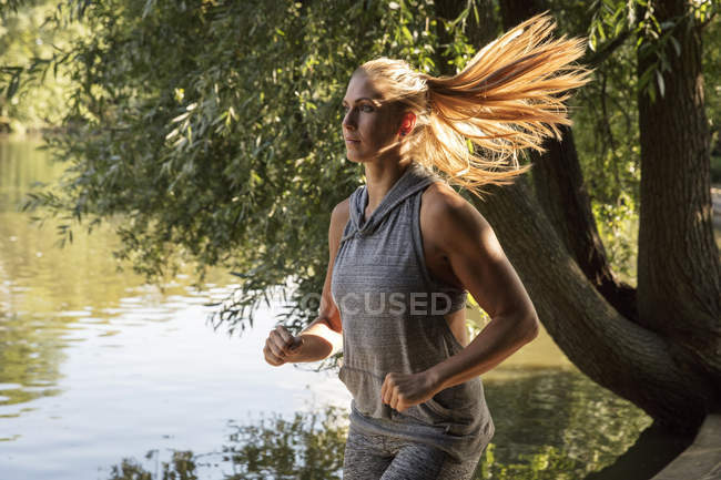 Молода жінка біжить біля паркового озера — стокове фото