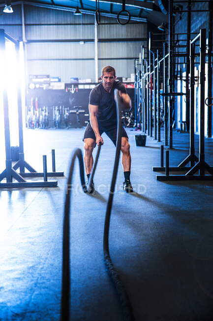 Man exercising in gym, using battle ropes — Stock Photo