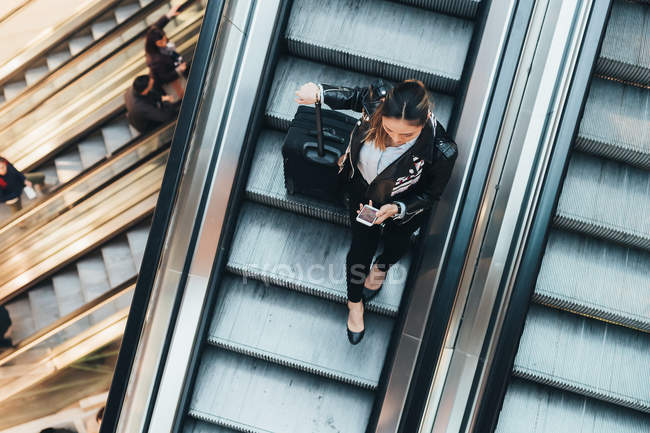 Mujer en escalera mecánica sosteniendo maleta - foto de stock