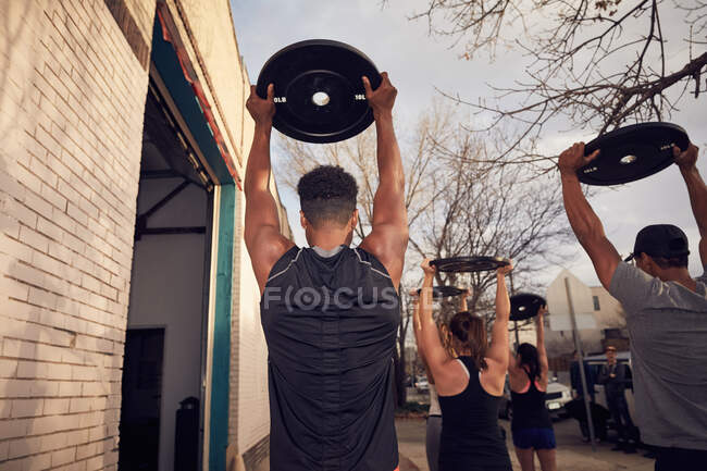 Rear view of people with arms raised carrying weights equipment — Stock Photo