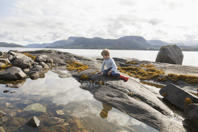 Boy looking at fjord rockpool, Aure, More og Romsdal, Noruega - foto de stock