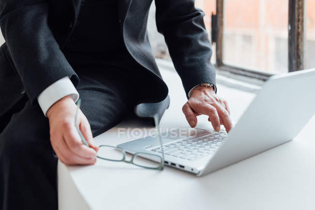 Empresario sentado en el alféizar de la ventana usando el ordenador portátil, recortado - foto de stock