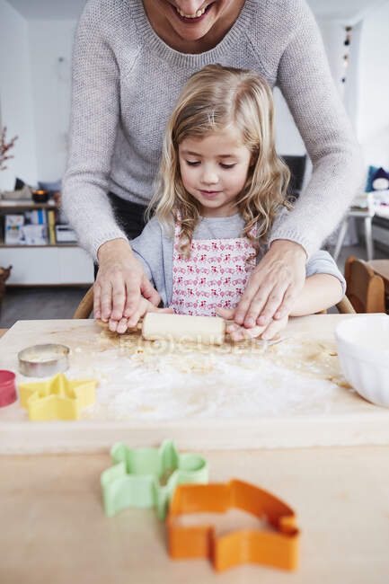 Mãe ajudando filha rolar massa de biscoito na mesa da cozinha, seção meados — Fotografia de Stock
