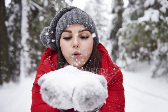 Jovem mulher soprando flocos de neve fora das mãos — Fotografia de Stock