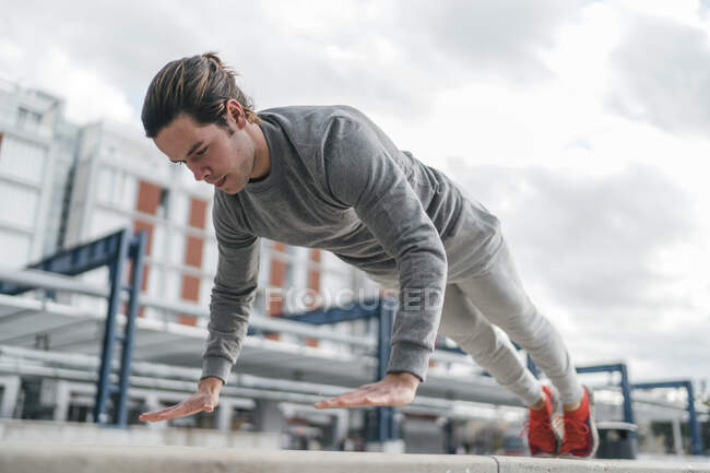 Young man training, doing push up in city, low angle view — Stock Photo