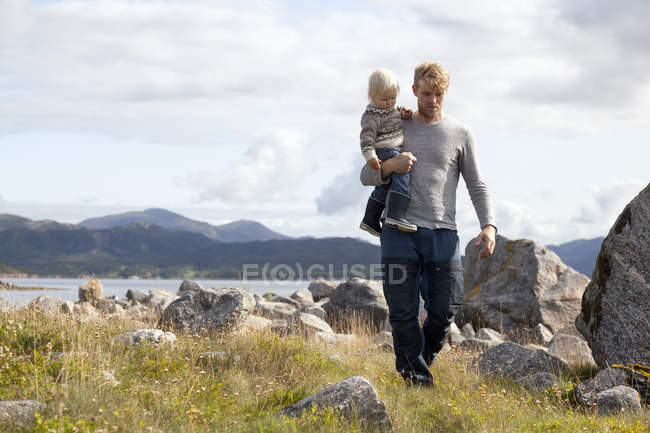 Hombre llevando hijo por fiordo, Aure, More og Romsdal, Noruega - foto de stock