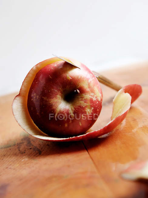Une pomme rouge avec écorce et couteau sur la table — Photo de stock